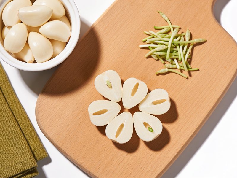Mitades de ajo limpias en un tazón pequeño junto a un montoncito de gérmenes verdes en la tabla.