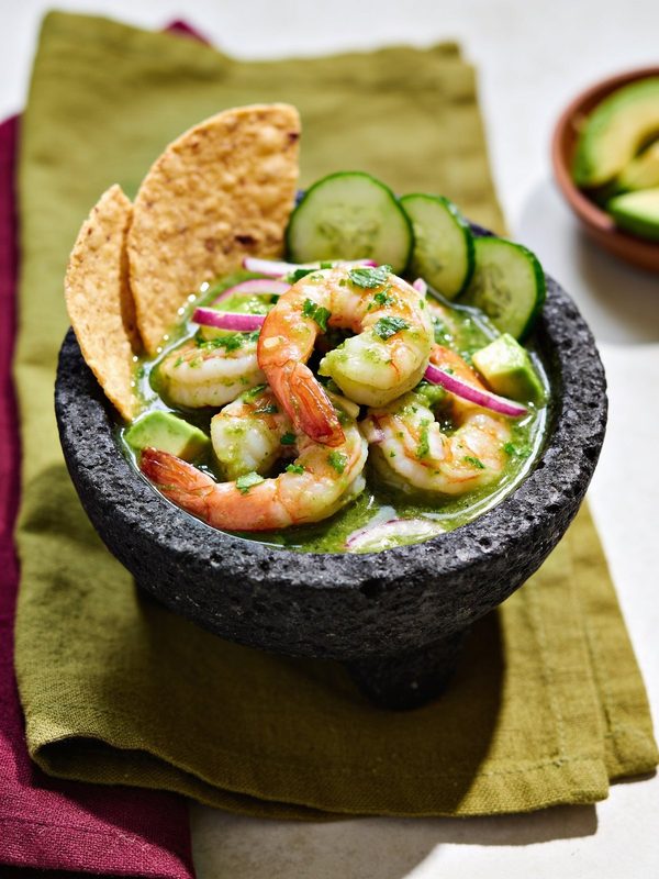 Green aguachile with pink shrimp, cucumber, red onion and avocado in a stone molcajete, with tostada chips.