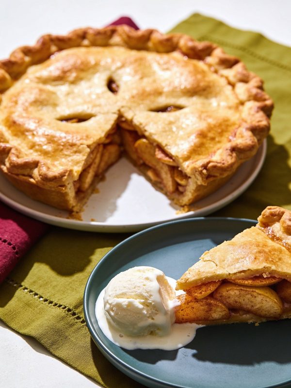 A golden double-crust apple pie with one slice served on a plate with vanilla ice cream.