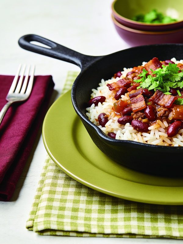 A cast iron skillet of white rice with stewed red kidney beans and crispy bacon pieces, topped with fresh cilantro.