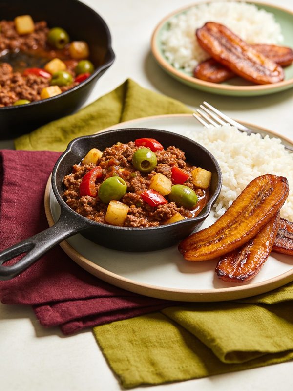 Beef picadillo with olives and diced potatoes next to white rice on a plate.