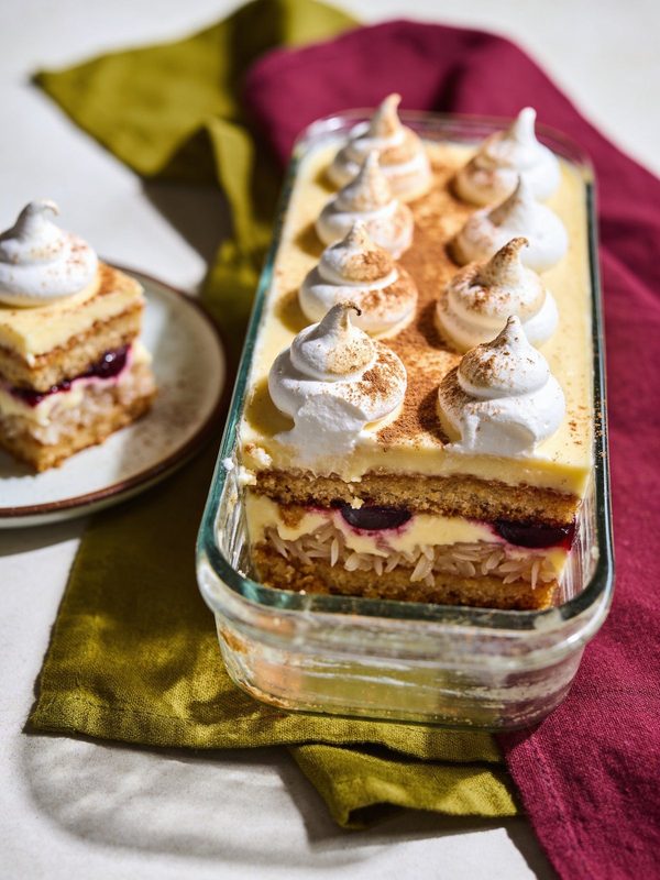 Layers of sponge cake and coconut cream in a glass dish, topped with meringue kisses dusted with cinnamon.