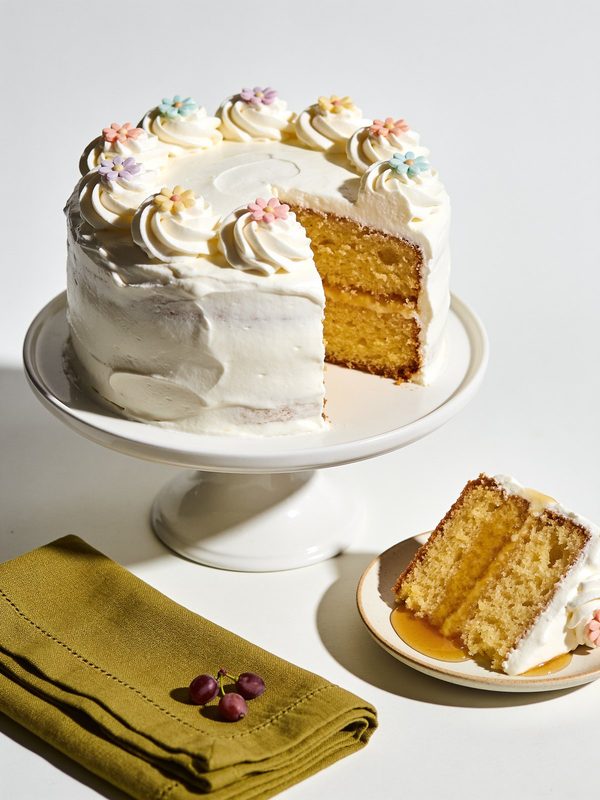 A tall round Puerto Rican bizcocho mojadito covered in glossy white meringue frosting with small sugar flowers, one slice cut to show the moist golden crumb.