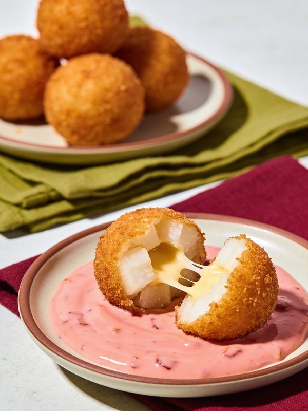 Golden fried yuca balls, one pulled open to show soft yuca and stretchy melted cheese, with pink mayo-ketchup.