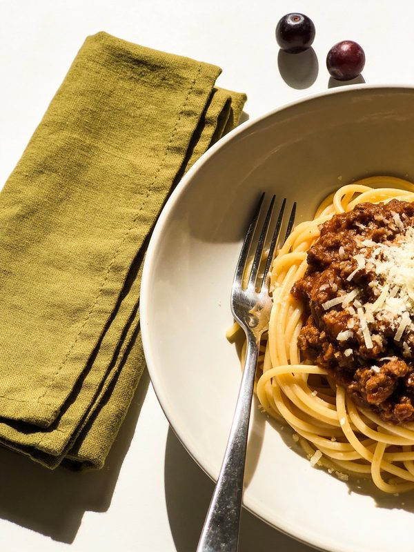Spaghetti topped with a rich meat bolognese sauce and grated parmesan in a shallow bowl.