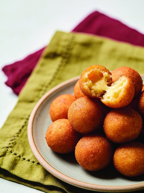 Round golden fried cheese fritters on a plate, one broken open to show a soft, cheesy inside.