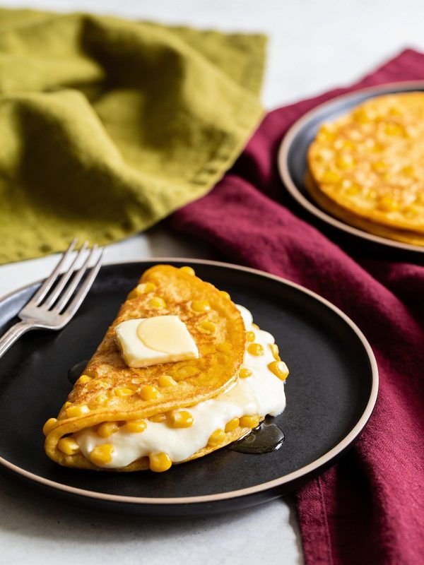 A folded golden corn cachapa filled with melted white cheese and topped with a pat of butter.