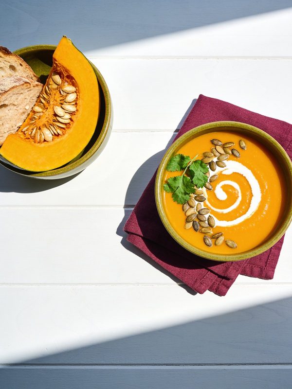 A bowl of bright orange calabaza soup with a swirl of coconut milk, pumpkin seeds and cilantro.