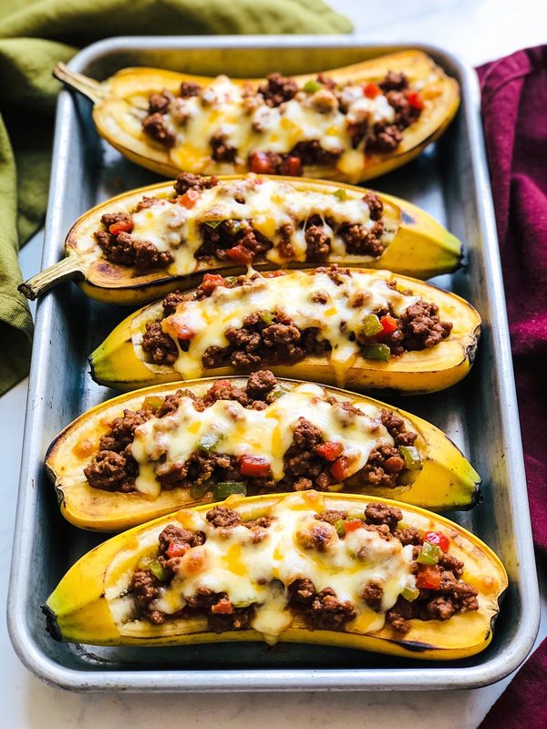 Ripe plantain boats in their skins on a baking tray, stuffed with beef picadillo and diced peppers and topped with melted cheese.