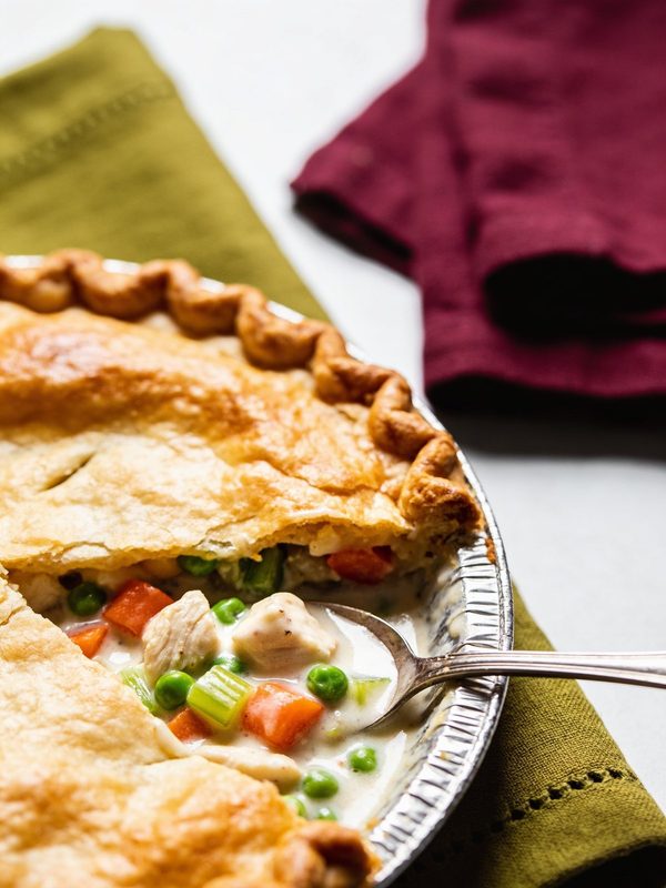 A golden chicken pot pie with a crimped crust, a slice taken out to show chicken, peas, carrots and celery in a creamy white sauce.