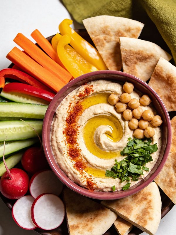 A plate of smooth hummus with a swirl of olive oil, paprika and parsley, with pita on the side.