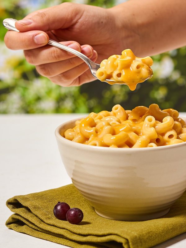 A bowl of creamy elbow macaroni coated in a smooth cheddar cheese sauce, with a spoon lifting a cheesy bite.