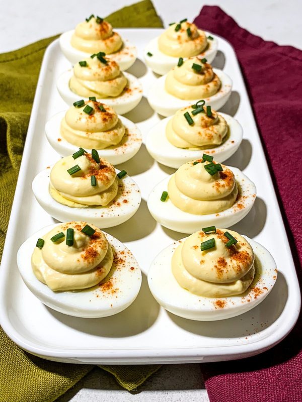 Deviled eggs with piped yolk filling, paprika and chives in neat rows on a white platter.