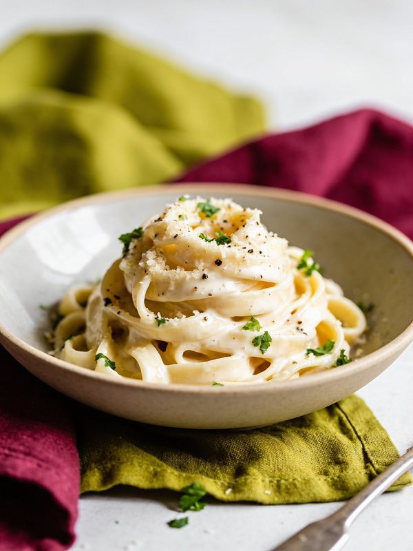 Fettuccine twirled in a shallow bowl, coated in a creamy white Parmesan sauce with cracked black pepper, grated cheese and chopped parsley.