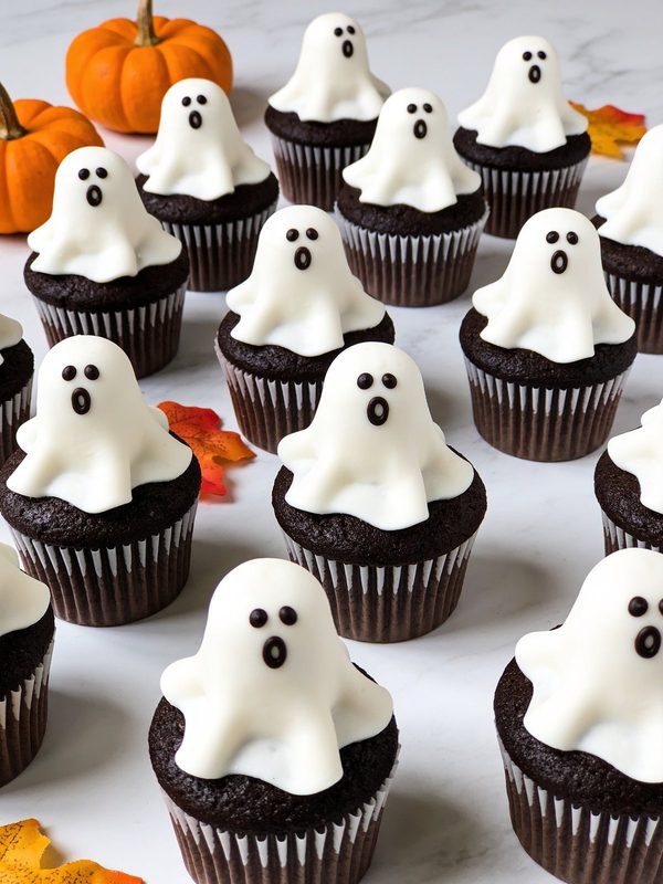 Rows of chocolate cupcakes topped with tall white frosting ghosts with little black eyes and O-shaped mouths.