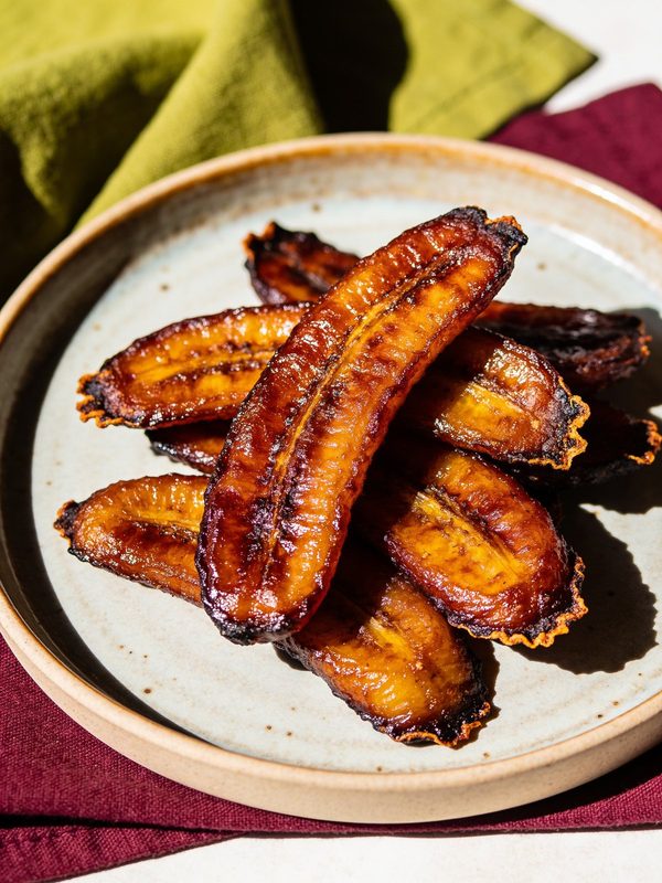 A plate of caramelized fried ripe plantain slices with dark, crisp edges.