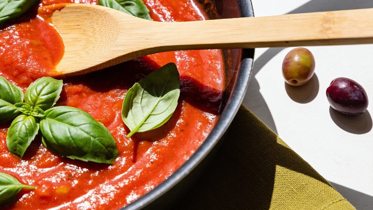 Una olla de salsa marinara de un rojo intenso con hojas de albahaca fresca y una cuchara de madera.