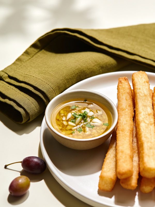 A small bowl of golden garlic mojo with olive oil, minced garlic and parsley, next to fried yuca.