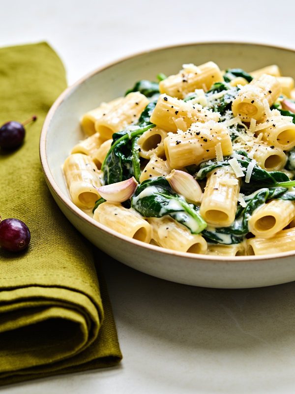 Creamy penne with wilted spinach and grated parmesan in a white bowl.