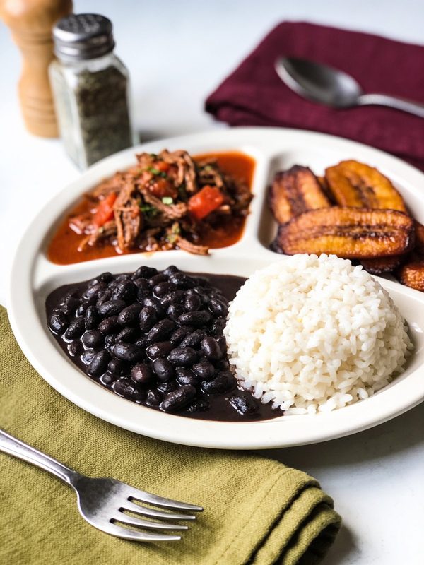 A pabellón criollo plate with shredded beef in tomato sauce, black beans, white rice and fried sweet plantains.