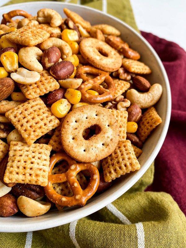 A large bowl of toasted savory snack mix with cereal squares, pretzels, round crackers and mixed nuts.