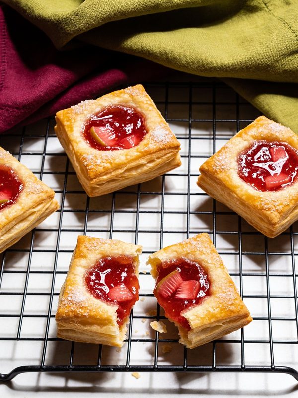 Square puff pastry tarts with a glossy red guava filling and guava pieces, sprinkled with sugar, on a cooling rack.