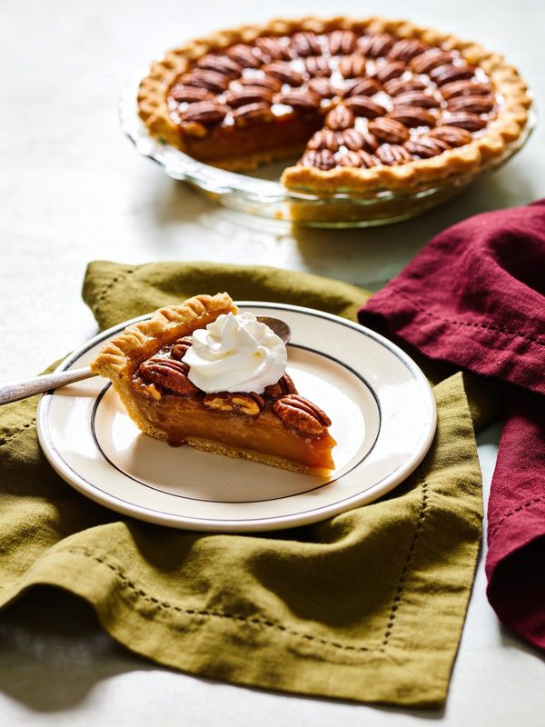 A pecan pie with rings of pecan halves, with one slice on a plate topped with whipped cream.