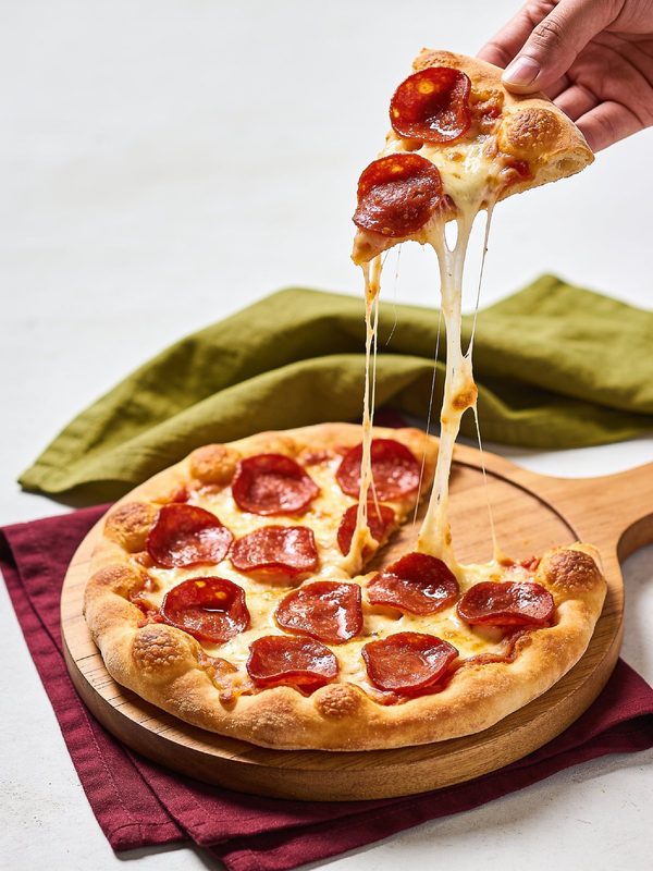 A pepperoni pizza with a puffy golden crust on a wooden board, with a slice lifted away in a long stretch of melted mozzarella.