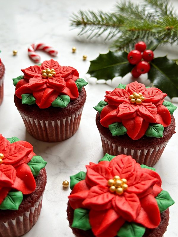 Red velvet cupcakes topped with piped red buttercream poinsettias, green leaves and golden sugar pearl centers.
