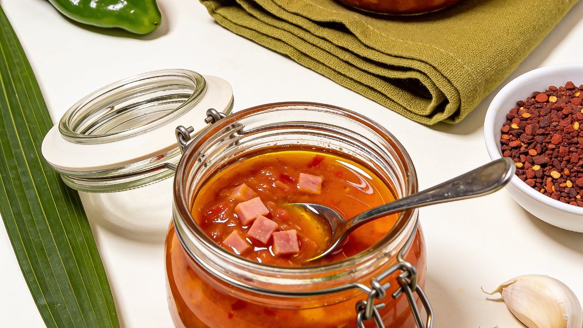 Frasquitos de cristal con sofrito puertorriqueño anaranjado con pedacitos de jamón, brillante por el aceite de achiote, con ajíes dulces, hojas de recao y ajo al lado.