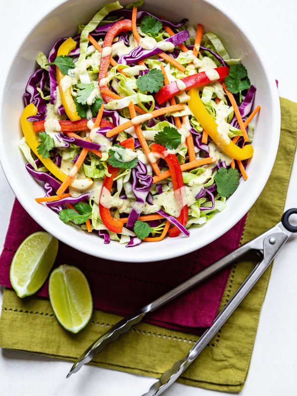A bowl of colorful slaw with purple and green cabbage, carrot, red and yellow bell pepper and cilantro.