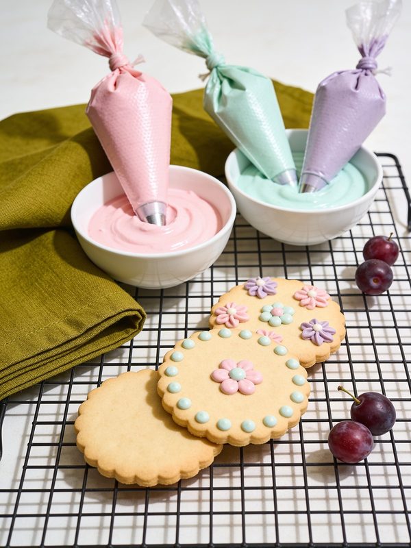 Tazoncitos de glasé real en rosado, verde menta y lavanda con mangas pasteleras, junto a galletas decoradas.