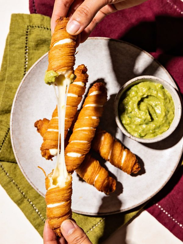 Golden tequeños with a stretchy cheese pull and a bowl of green guasacaca on the side.